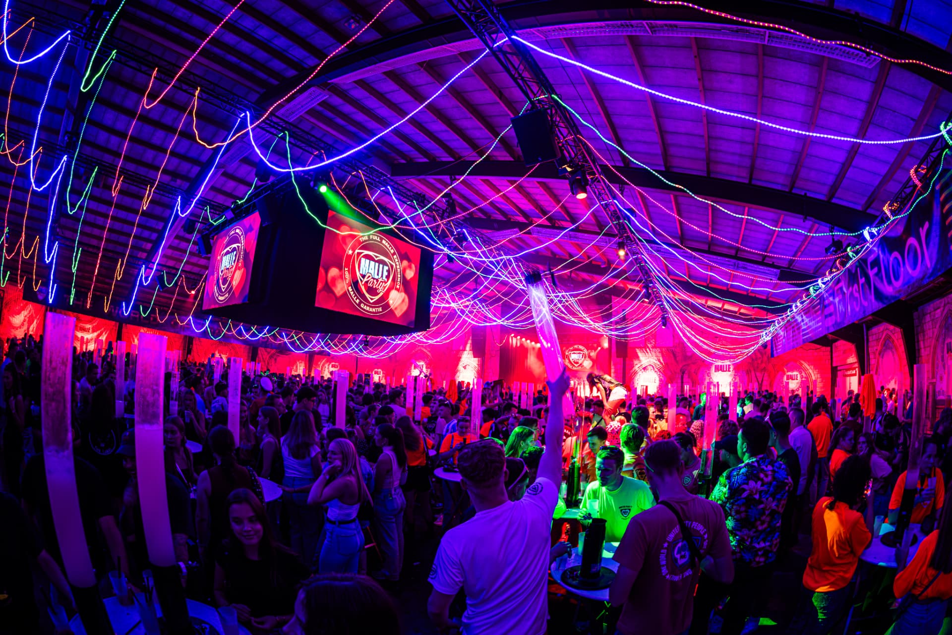 Drukke Malle Party-feestzaal met publiek en kleurrijke neonverlichting